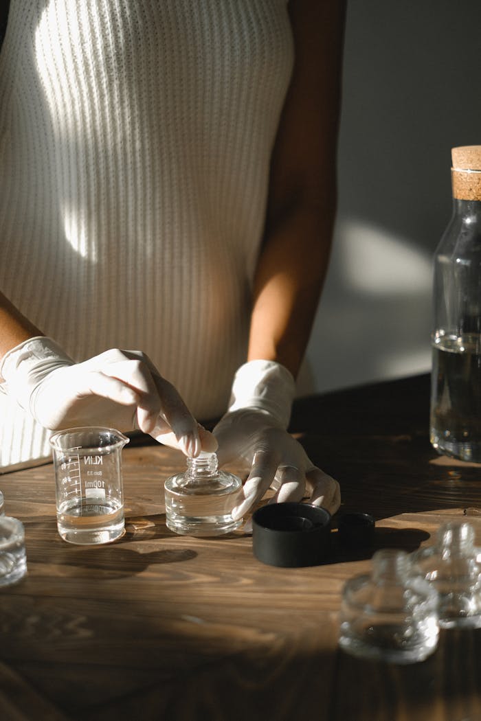 Crop faceless black female standing at table with glass bottles and preparing liquid incense using essential oils